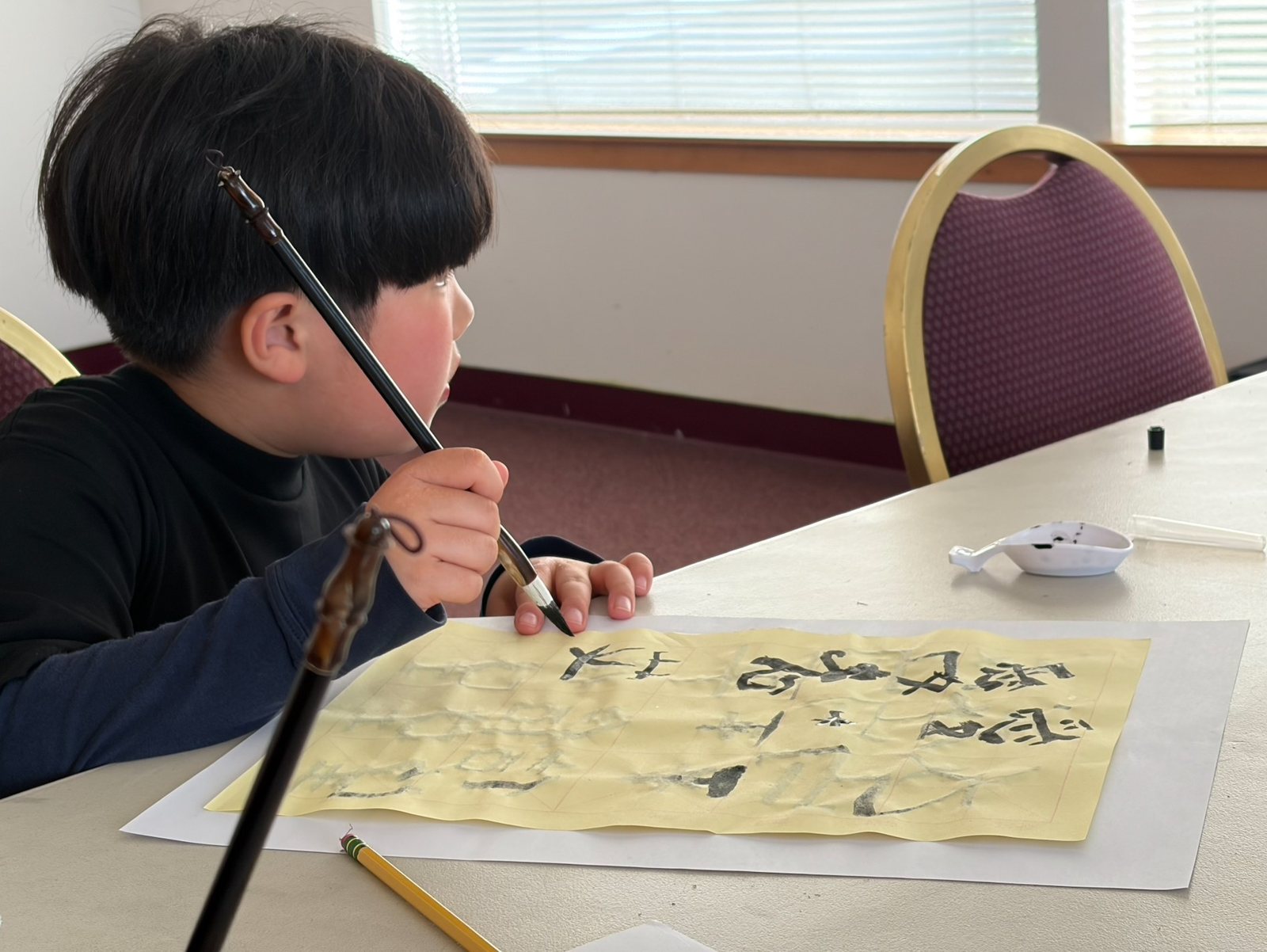 A boy writes with a brush on practice paper at the calligraphy table