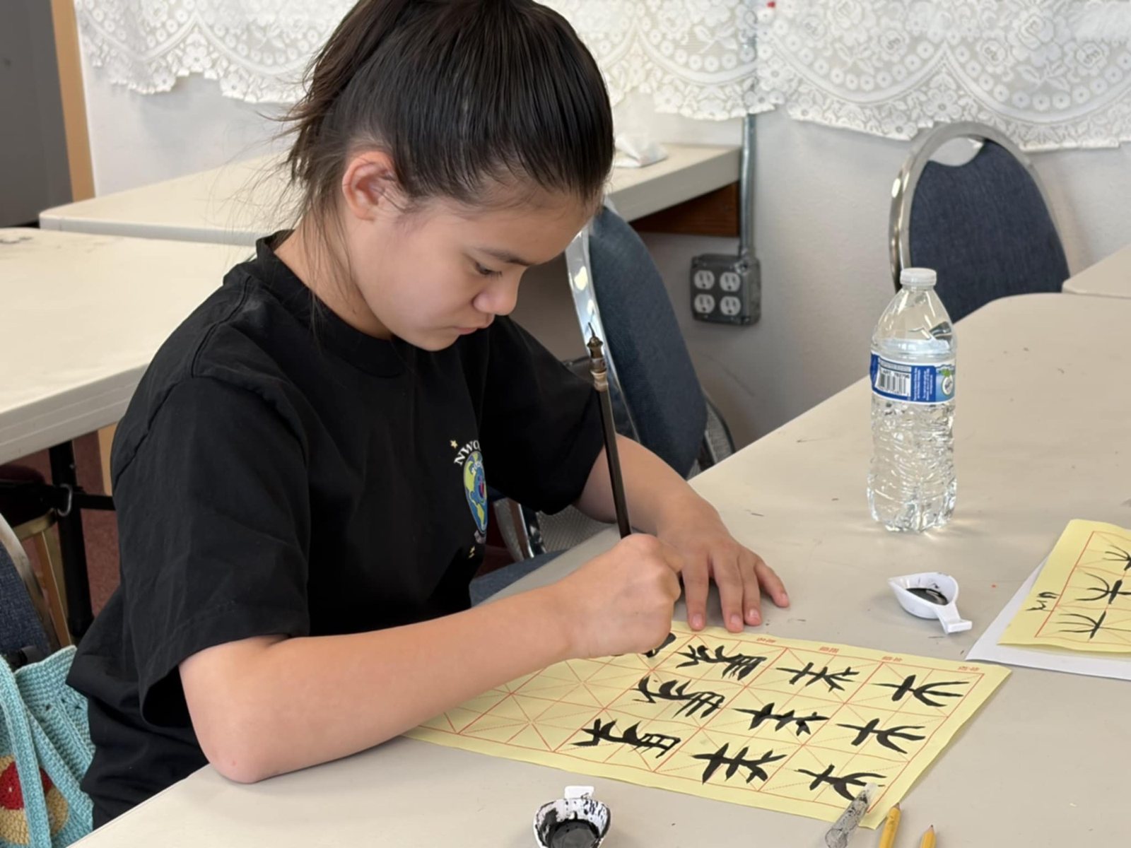 A girl in a black shirt writes with a brush
