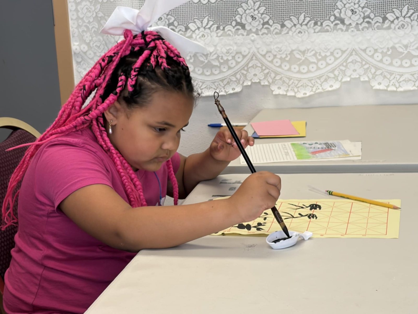 A girl dips her brush while writing at the calligraphy table