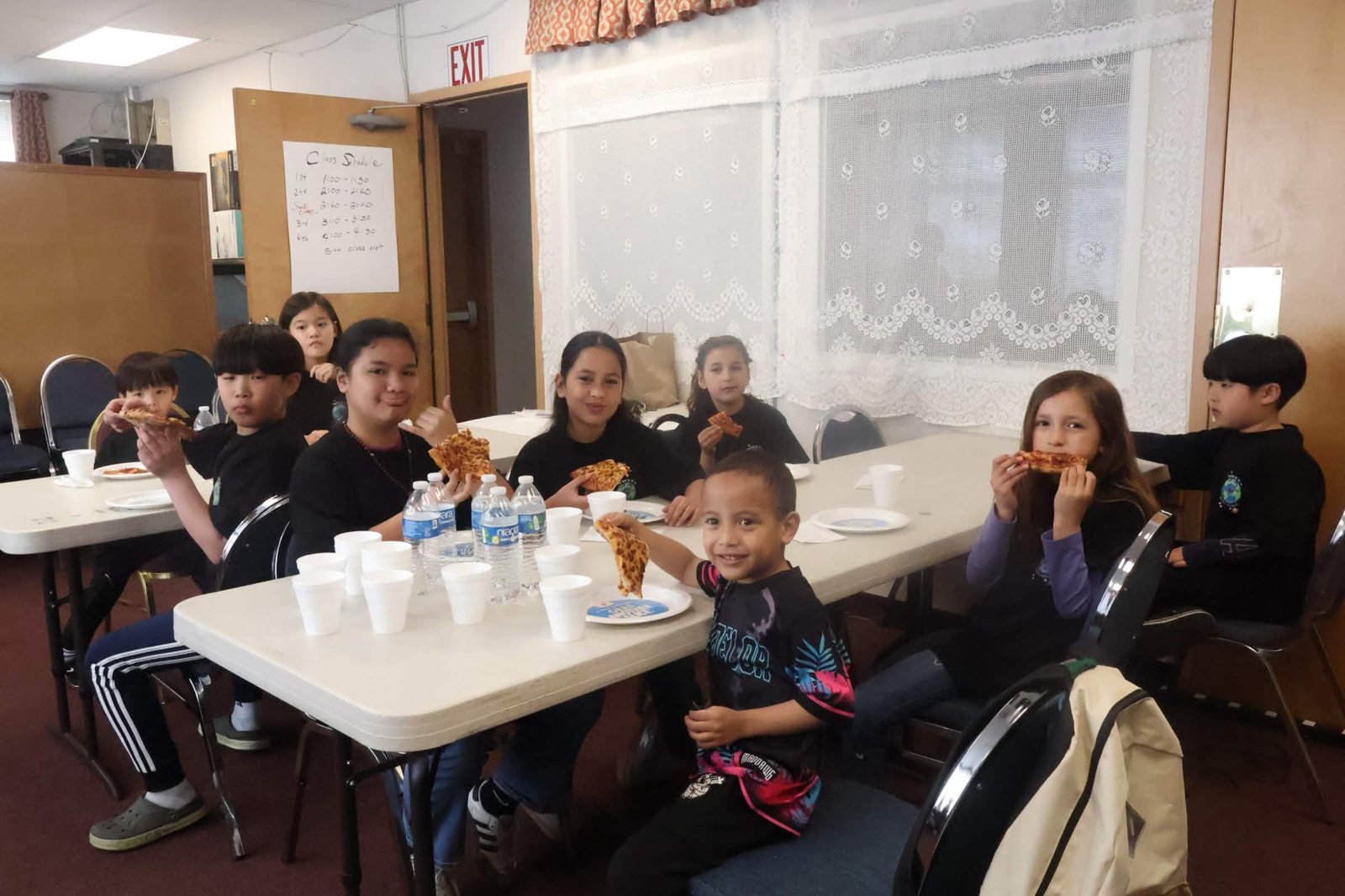 Children eat pizza at a long table in the classroom