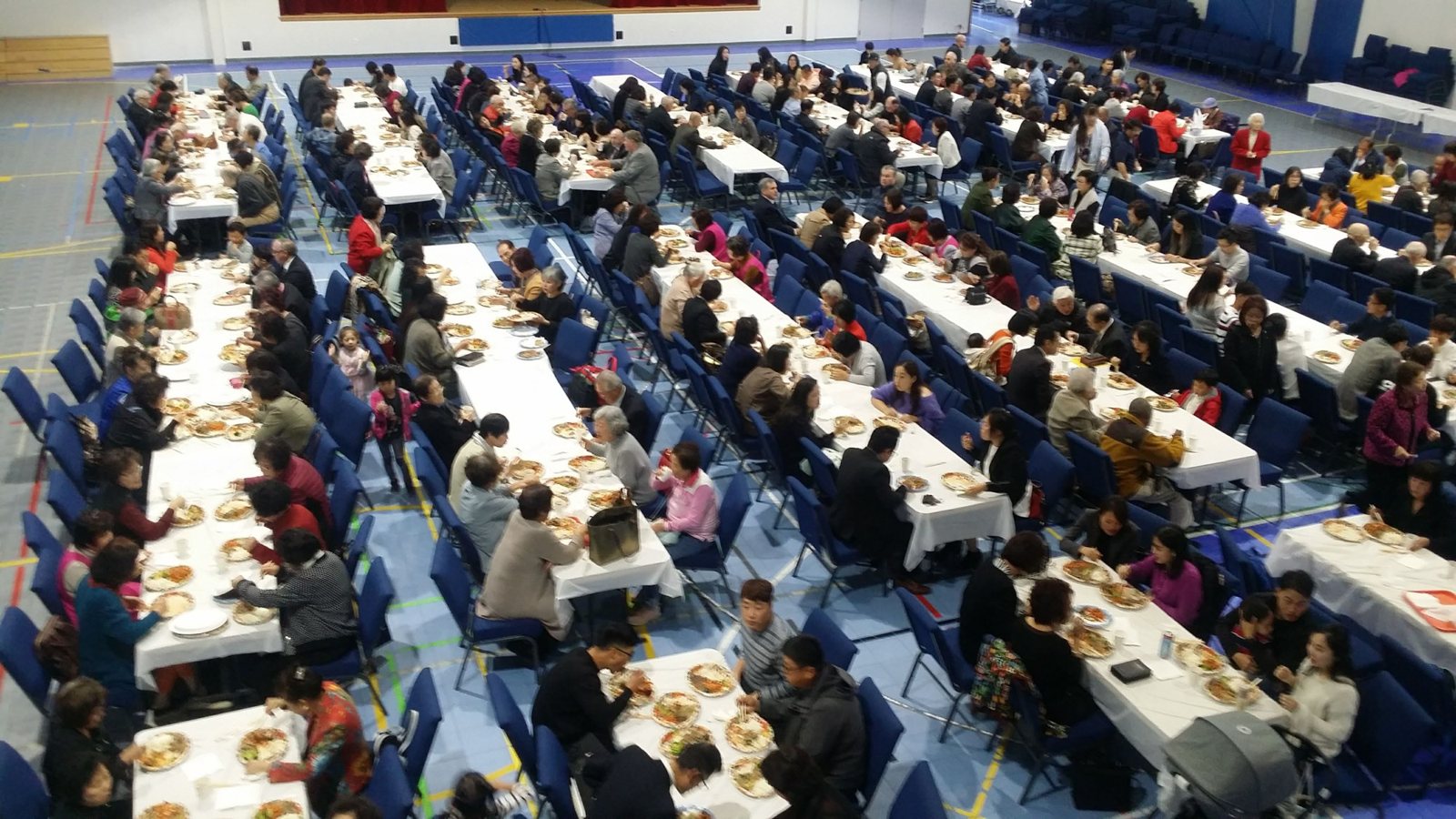 Long tables of guests at a community meal in the hall, seen from the balcony