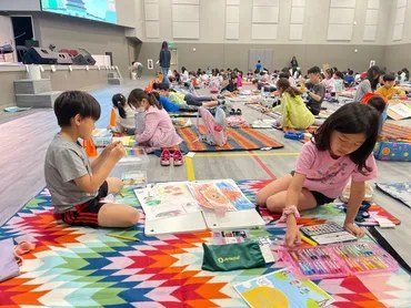 Children sit on patterned mats in the hall working on crafts