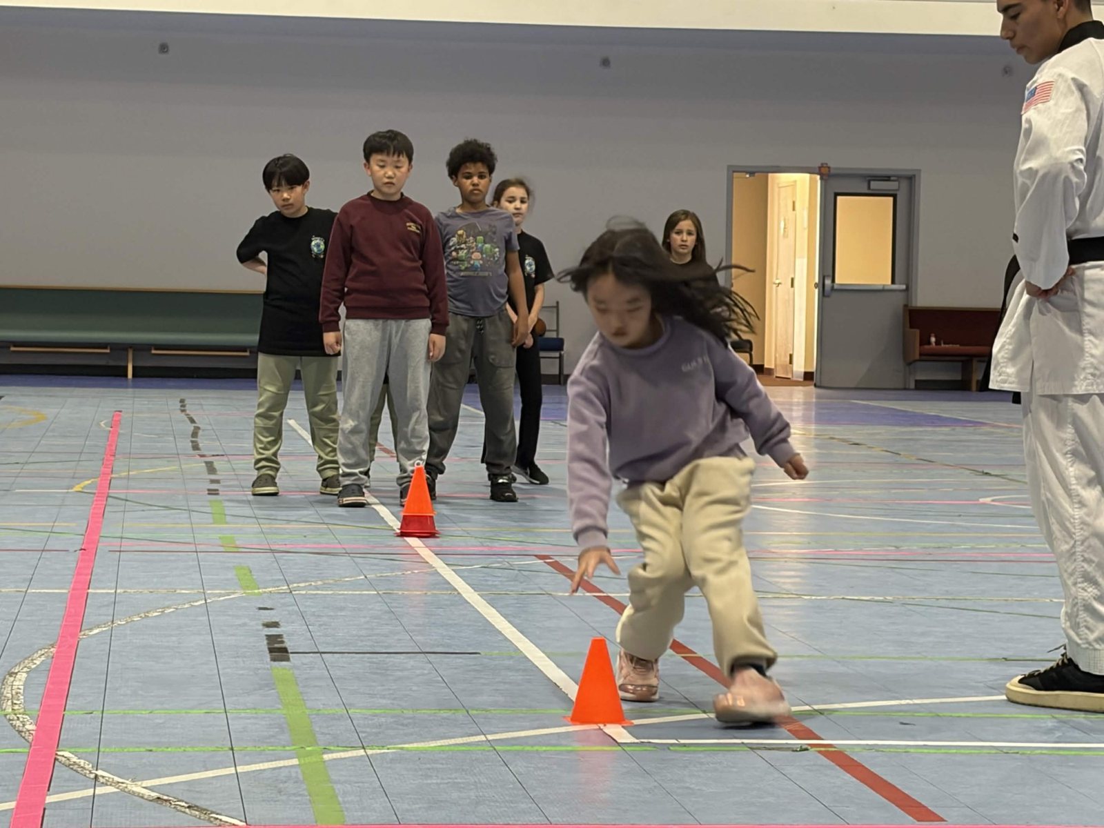 Children run a relay around orange cones in the gym
