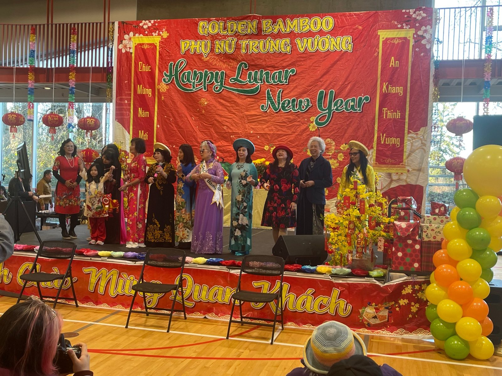 Performers in costume on a stage decorated with a Happy Lunar New Year banner